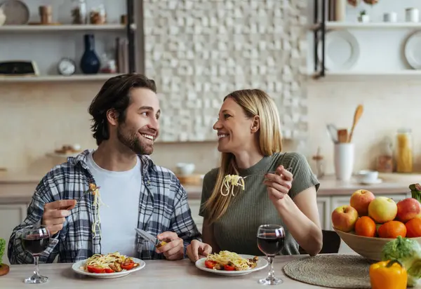 Mutlu Avrupalı bin yıllık sarışın eş ve açık mutfak mutfağında sakal yiyen makarna eşliğinde gülerek. Evde romantik bir akşam yemeği, aşk, ilişki ve aile salgını.