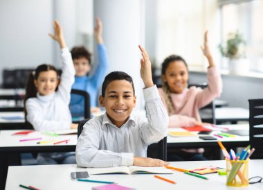Eğitim, İlkokul, Öğrenme ve İnsanlar Konsepti. Çeşitli ortaokul öğrencileri sınıflarında oturmuş, cevap almak için ellerini kaldırıyor ve zevkle ders çalışıyorlar.