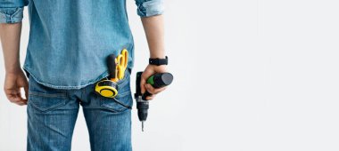 Erkekler çalışıyor, ev tadilatı, inşaat ya da marangozluk işi. Kot pantolonlu genç adam cebinde aletlerle elektrikli matkap tutuyor, beyaz arka planda izole edilmiş, panorama, boş alan, kırpılmış, arka