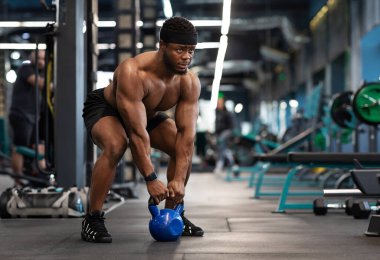 Spor salonunda kettlebell ile egzersiz yapan, fotokopi alanına bakan kaslı Afro-Amerikan vücut geliştirici. Atletik siyah adam ağırlık kaldırıyor ya da ağırlık kaldırıyor, vücut kasları üzerinde çalışıyor.