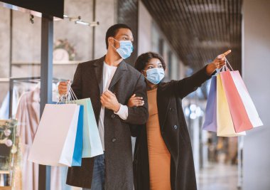 Alışveriş zamanı ve düşük fiyata inanılmaz bir indirim. Genç nesil Afro-Amerikan ailesi koruyucu maskeli birçok çanta taşıyor. Kara Cuma Covid-19 salgını sırasında kadınlar butikte gösteriler yapıyor.