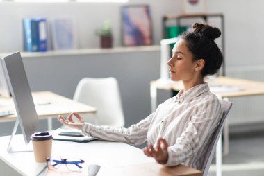 İşte stresle başa çıkmak. Genç Latin ofis çalışanı yoğun bir günün ardından işyerinde meditasyon yapıyor, nefes egzersizleri yapıyor. İşyeri stres yönetimi