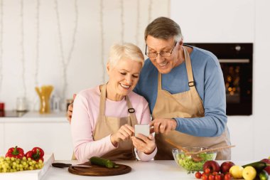Yemek Uygulaması. Modern mutfaktaki Akıllı Telefon Hazırlama Yemeği 'ni kullanan mutlu son sınıf çifti. Evde Cep Telefonu İnternette Tarifi Arayan Yaşlı Eşler.