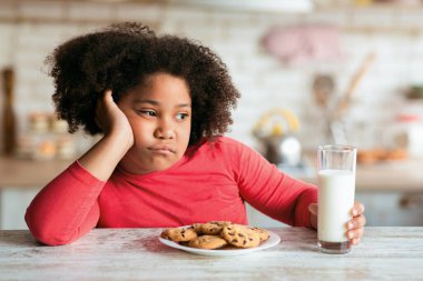 Süt ve kurabiyelerle masada oturan sıkkın siyah kız kahvaltı yapmayı reddediyor, mutsuz çocuk kafasında dinleniyor ve uzaklara bakıyor, iştahsız yaramaz çocuk mutfakta oturuyor,