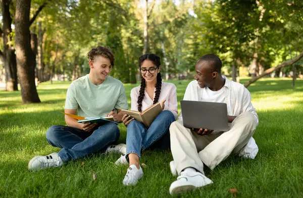 Çeşitli öğrenci arkadaşlar öğreniyor, kitap okuyor, dizüstü bilgisayar kullanıyor ve üniversitenin kampüs parkında bir şeyler tartışıyorlar. Dışarıda çimlerde oturuyorlar.