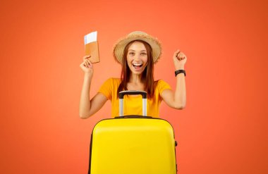 Pasaportu ve uçak biletleri olan heyecanlı genç bayan turist sarı stüdyo geçmişine el kaldırıyor. Elinde bavuluyla gülümseyen bayan gezginler için harika bir anlaşma seçiyor. Tatil, yolculuk kavramı