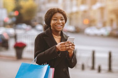 Satış sezonunun başlamasıyla ilgili mesaj ve mobil uygulamadan alışveriş koliği için Kara Cuma. Mutlu bin yıllık Afro-Amerikan kadınları ellerinde renkli çantalar, akıllı telefonlar ve alışverişe hazırlar.