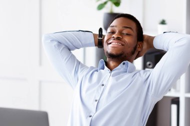 Mutlu Afro-Amerikalı adam koltuğunda dinleniyor, ofisteki dizüstü bilgisayarının önüne yaslanıyor, başarılı bir iş anlaşmasından sonra dinleniyor veya internet konferansından sonra, fotokopi çekiyor. İş yerinde neşeli siyah yönetici