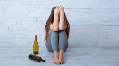 Alkolizm ve depresyon kavramı. Genç bir kadın evinin zemininde boş şişelerle ağlıyor. Kadın alkol bağımlısı kendini çaresiz hissediyor. Üzüntülerini şaraba boğuyor.