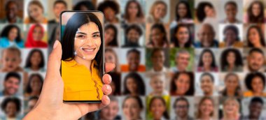 Bir kişi elinde yüzünün yüz tanıma taramasını gösteren bir akıllı telefon tutuyor. Arka planda çeşitli yüzlerden oluşan bir kolaj yer alıyor, tanımlamada teknolojinin uygulamasını gösteriyor.