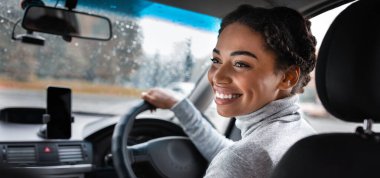 Harika bir yolculuk, araba yolculuğu ve şehirde iyi yolculuklar. Mutlu genç Afrikalı Amerikalı kadın sürücü arka koltukta yolcu koltuğuna dönüyor. Şehir yolu görüntüsü, yağmur damlalı pencere ve akıllı telefon, boşluğu kopyala