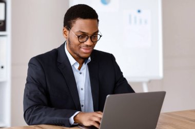 Resmi takım elbiseli, dizüstü bilgisayarla çalışan, gözlük takan, ofis içi, fotokopi odası takan gülümseyen genç siyahi girişimci. Başarılı bin yıllık Afro-Amerikan iş adamı iş projesi üzerinde çalışıyor.