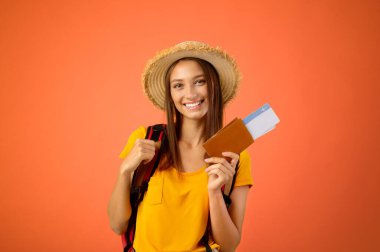 Pasaportu ve uçuş biletleri olan neşeli bir kadın. Tatile hazırlanıyor. Stüdyoda sarı bir geçmişi var. Gülümseyen genç bayan yolcu uçak biletlerini aldı, aktif istirahat, seyahat, turizm...