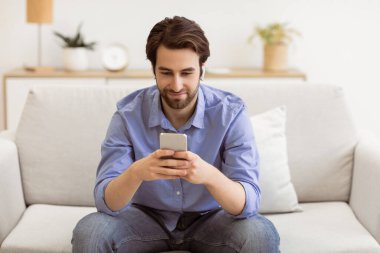 Kulaklık takan, interneti kolaçan eden ve evdeki koltukta oturup müzik dinleyen bir adam. Oturma odasında akıllı telefondan mobil kullanıcı mesajı. Cep telefonu Uygulaması Konsepti