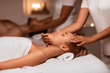 Lüks Spa 'da rahatlatıcı yüz masajı yapan, güzellik prosedürü sırasında gözleri kapalı yalan söyleyen bir çift. Sağlık, Rahatlama Terapisi ve Gençleştirme Konsepti. Seçici Odaklanma, Düşük Işık