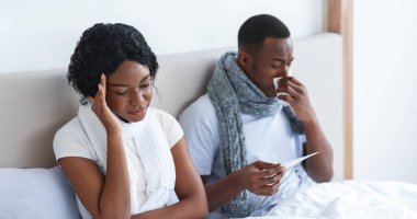 Hasta Afrikalı Amerikalı çift yatak odasında yatakta eşarba sarılmış, ateşi ölçüyor ve burunları aksıyor. İki kişilik genç zenci aile hastalandı, evde kaldılar, mevsimlik virüsler ve grip konsepti.