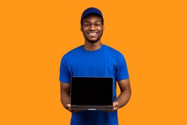 Siparişinizi izleyin. Sırıtkan siyah teslimatçının portresi elinde boş ekranla mavi başlık ve üniforma giyerek turuncu arka planda boş monitörlü bilgisayarı gösteriyor.