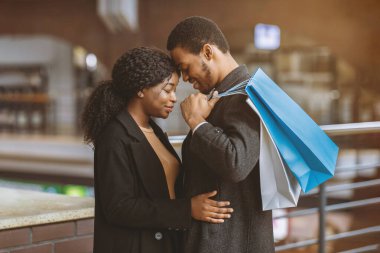 İki kişilik romantizm, mevsimsel satışlar ve Kara Cuma sırasındaki şefkat ve tarih. Siyahi alışveriş çantalarına aşık genç Afro-Amerikan çift alışveriş merkezinde kucaklaşmaya hazır, yan görüş, serbest alan