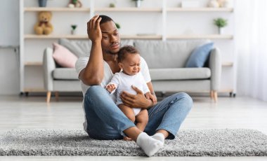 Blues Baba. Stresli genç siyah baba evde yerde ağlayan bebekle oturuyor, üzgün Afrikalı Amerikalı baba kafasına dokunuyor, ızdırap çeken babalık sorunları yaşıyor, kopyalama boşluğu dolduruyor.