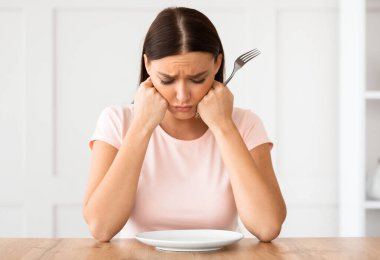 Diyet Konsepti. Mutsuz kadın boş tabağa bakıyor. Masada oturmuş kilo kaybediyor..