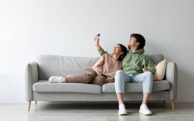 Sistemi ayır. Klima altında uzaktan dinlenen mutlu Asyalı çift, evdeki kanepede oturmuş, tasarım için maket yapıyorlar. Mutlu milenyum eşleri içeride iklim kontrolü kullanıyor.