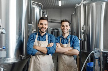 Favori işinde mutlu çalışanlar, küçük işletmeler ve erkek işleri. Kollarını kavuşturmuş önlüklü neşeli genç işçiler fabrikanın iç kısımlarındaki büyük kazanlı kameralara, boş alana bakıyorlar.