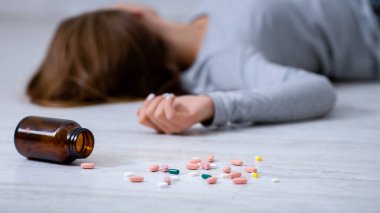 Genç bir kadın aşırı dozda hap alarak intihar ediyor. Yere saçılmış bir şişe tablete odaklan. Depresyon ve aşırı uyuşturucu kullanımı, zihinsel çöküntü veya travma sonrası stres bozukluğu sorunu kavramı