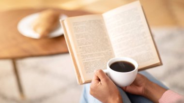 Kahve kitabı okuyan tanınmayan siyahi kadın, evde huzurlu bir sabah geçiriyor, boş bir alan. Hafta sonları elinde sıcak içecek ve ders kitabı tutan kadınların kapalı mekanları.