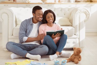 Doğum konseptine hazırlanıyorum. Hamile siyah çift, doğum hastanesine gitmeden önce bebek eşyalarının listesini yapıyor. Sevgi dolu koca, doğum merkezi için çocukça şeyler not alıyor.