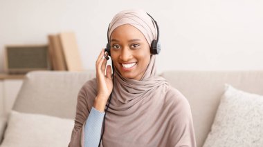 Başörtülü Müslüman iş kadını, merkez ofisteki bilgisayardaki meslektaşlarıyla çevrimiçi görüşmede notlar alıyor. Kulaklıklı olumlu Arap bayanın internet sitesi ya da konferansı var.