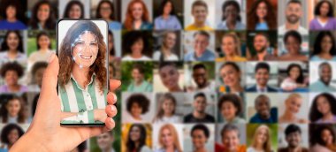 Bir el, yüz tanıma taraması yapan bir akıllı telefonu tutuyor. Arka planda birden fazla portre beliriyor, tanımlama amacıyla modern teknolojinin uygulamasını sergiliyor.