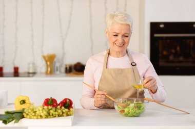 Modern Mutfak 'ta Yemek Hazırlayan Yaşlı Kadın. Sağlıklı sebze salatası yapan yaşlı kadın kasedeki malzemeleri karıştırıyor. Beslenme ve Tarifler Konsepti
