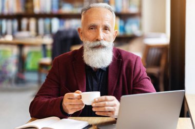 Uzun gri sakallı yakışıklı yaşlı bir adam sabah kahvesini kafeteryada içerken, masada dizüstü bilgisayar ve defterle oturup, fotokopi çekerken. Kıdemli işadamı not alıyor ve internette çalışıyor.