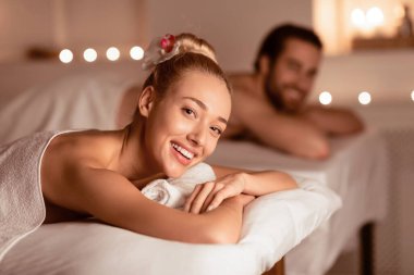 Rahatlamış Kadın Rahatlatıcı Güzellik Prosedürünü Kocasıyla Spa Resort 'ta Yatmak, Kameraya Gülümsemek. Aromaterapi, Sağlık ve Rahatlama, Balayı Eğlence Konsepti. Seçici Odaklanma