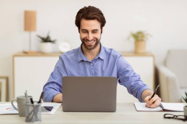 Başarılı bir iş adamı, modern ofiste dizüstü bilgisayarın başında oturup not alıyor. Profesyonel Meslek, Girişimcilik ve İş Kariyeri Konsepti. Seçici Odaklanma