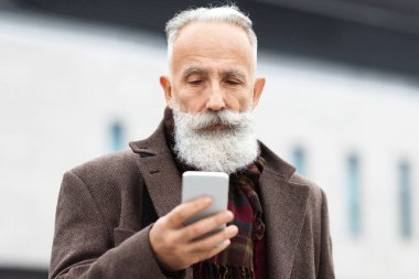 Zengin kıdemli bir adam, sokaklarda yürürken modern akıllı telefonunu kontrol ediyor. Yakışıklı, gri saçlı iş adamı işten eve geliyor, cep telefonu ekranına bakıyor.