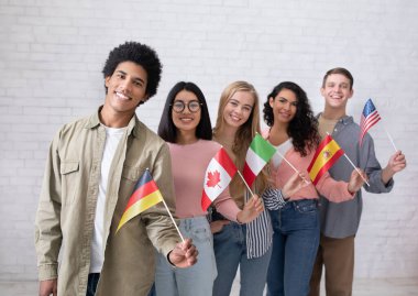 Uluslararası öğrencilerin ya da göçmenlerin modern eğitimi. Mutlu nesil z çok ırklı insanlar farklı ülkelerde bayraklar sallıyor üniversite sınıfında beyaz duvar arkasında, stüdyo çekimlerinde, boş alanlarda