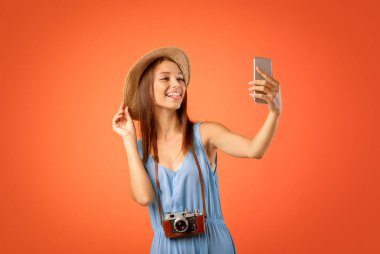 Güzel kız gezgin cep telefonuyla selfie çekiyor, sarı stüdyo geçmişi var.