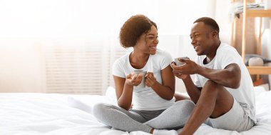 Genç, mutlu, Afro-Amerikan erkek ve kadın pijamalarıyla hafta sonunun tadını çıkarıyorlar. Evde birlikte oturup çay ya da kahve içip sohbet ediyorlar. Yatak odasının içi boş.