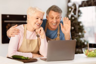 Laptop 'ta Noel tatilini uzaktan kutlayan ve mutfakta video görüşmesi yapan mutlu son sınıf çifti. Olgun Eşler Yılbaşı Yemeği Hazırlıyor ve Yeni Yıl 'da Uzaktaki Aile' yi Online Kutluyor