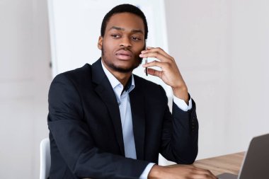 Düşünceli Afrikalı Amerikalı genç girişimci ofiste müşteri ya da iş ortağıyla telefon görüşmesi yapıyor, modern dizüstü bilgisayarla çalışıyor, işi hakkında kötü haberleri var, boşluğu kopyalıyor.