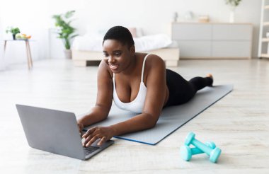 Artı, spor minderinde yatan, dizüstü bilgisayar kullanan, kişisel koçla konuşan ya da evde spor videosu izleyen boyunda bir zenci kadın. Kilolu milenyum bayanı antrenmana ara verdi.