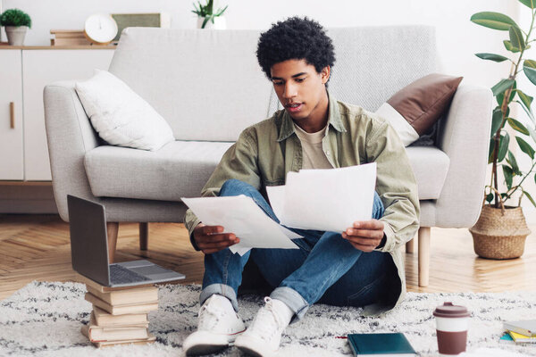 Концепция домашнего образования. Черный студент-подросток делает образовательный проект для своего онлайн-курса колледжа в помещении. Афроамериканский парень с документами, готовящимися к веб-конференции или дистанционному тестированию