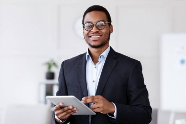 Elinde dijital tablet olan neşeli, genç siyahi bir menajer. Kameraya gülümsüyor. Ofis içi, fotokopi odası. Afrikalı Amerikalı işadamı iş başvurusunu ped üzerinde kullanıyor