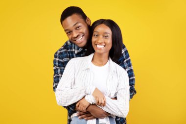 Mutlu romantik randevular ya da kendini yalnız bırakma. Neşeli genç Afro-Amerikan erkek ve kadın sıradan sarılıp kameraya bakıyorlar, sarı arka planda izole edilmiş, stüdyo çekimi, kopyalama alanı.