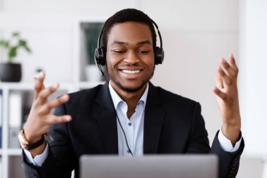 Kulaklığı olan, internet konferansı yapan, dizüstü bilgisayar kullanan, müşteri ya da iş ortağıyla konuşan, bilgisayar ekranına gülümseyen, ofisten yayın yapan siyahi iş adamlarının yakın çekimi.