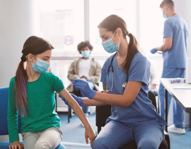 Aşı, bağışıklık sistemi, Hastalık Önleme Konsepti. Yüzünde maske olan genç bir kız sağlık merkezinde grip aşısı yaptırıyor. Profesyonel kadın doktor hastaya antiviral iğne yapıyor.