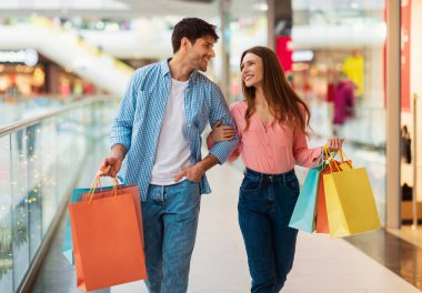 Başarılı bir alışveriş. Modern hipermarkette alışveriş torbaları taşıyan çift el ele tutuşuyor. Büyük Mevsimlik Satış Hafta Sonu 'nda Yeni Kıyafetler Alınıyor. Alışverişe ve ticarete