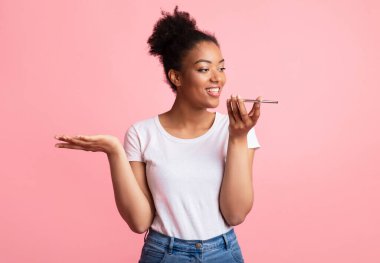 Akıllı telefonda ses asistanı kullanan mutlu genç siyahi bayan, Pastel Pembe Stüdyo Duvarı 'nın üzerinde izole edilmiş el kol hareketi yapıyor,