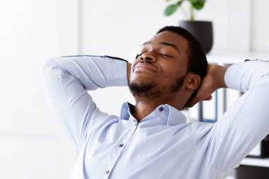 Modern ofisteki dizüstü bilgisayarının önünde koltuğuna uzanmış rahat Afro-Amerikan genç menajeri başarılı bir iş anlaşması ya da internet konferansından sonra dinleniyor.